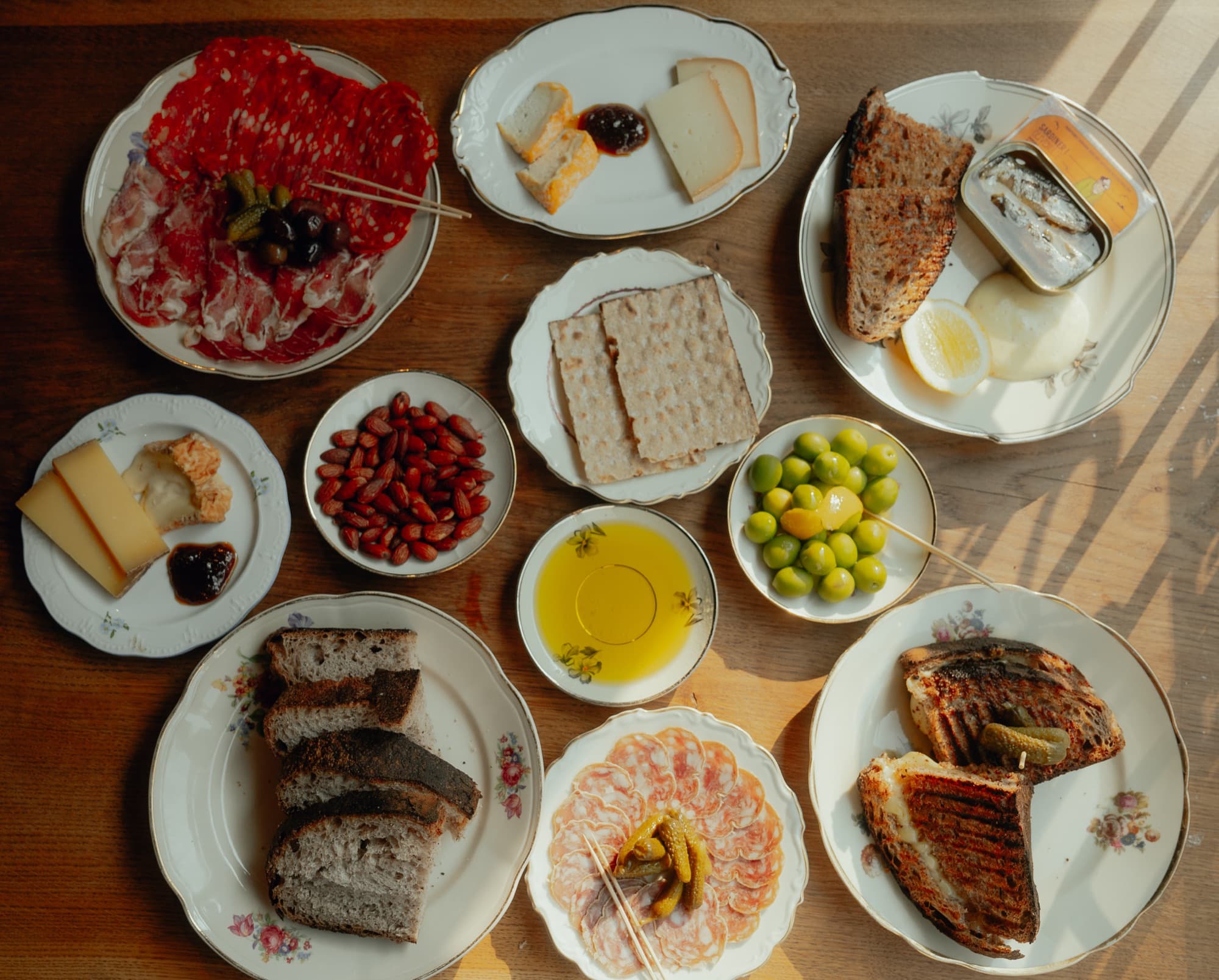 Bord dækket med ost, charcuteri, oliven, brød og en grillet sandwich