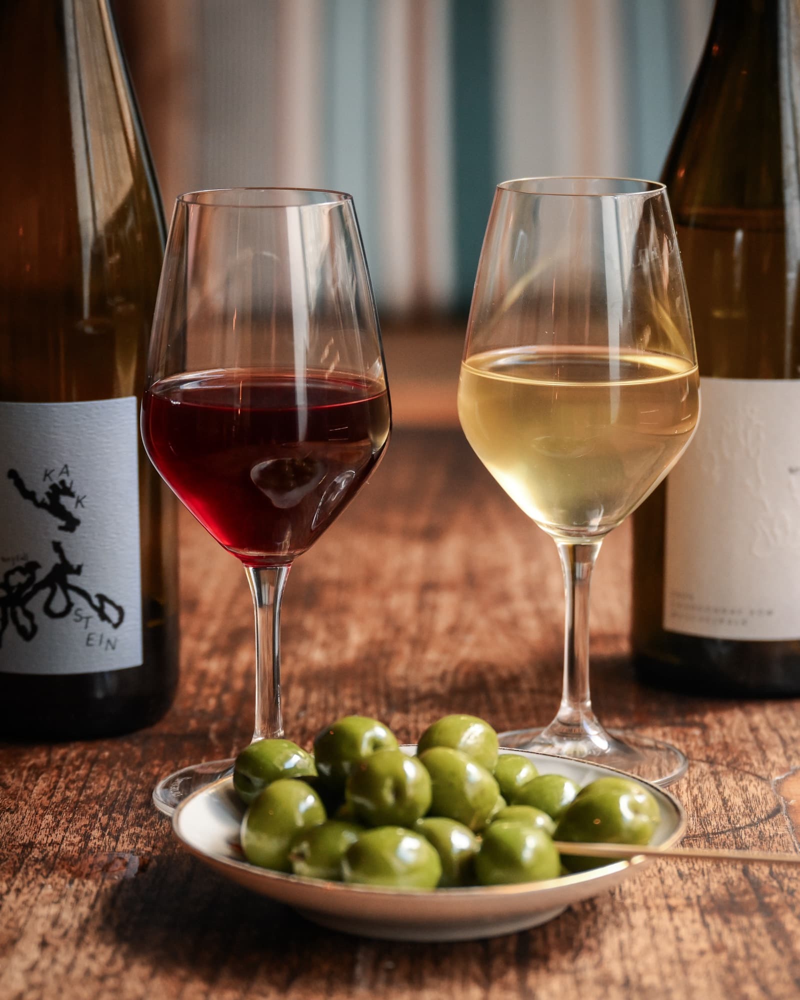 Et glas rødvin og et glas hvidvin på bordet med en skål oliven imellem